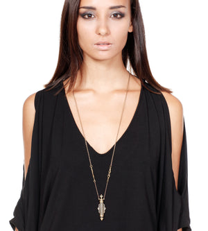 Woman wearing a black top and a long necklace with a pendant on a white background