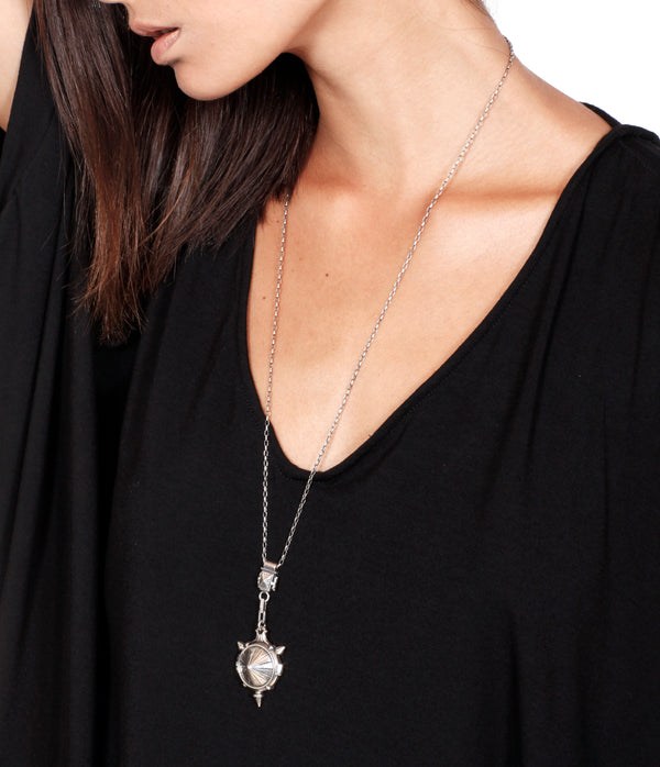 A person wearing a black V-neck top, displaying a silver prism locket pendant on a chain necklace.