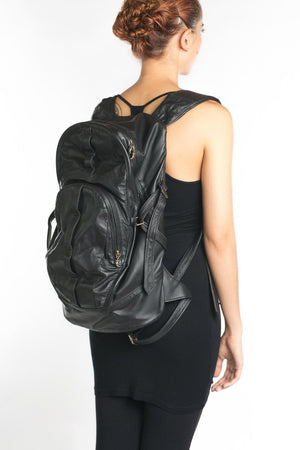 A person wearing a black leather backpack with a front pocket and adjustable shoulder straps.
