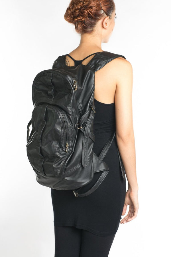 A person wearing a black leather backpack with a front pocket and adjustable shoulder straps.